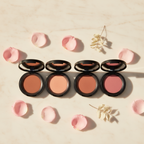 Compact blush in a black case surrounded by pink petals on a light marble background