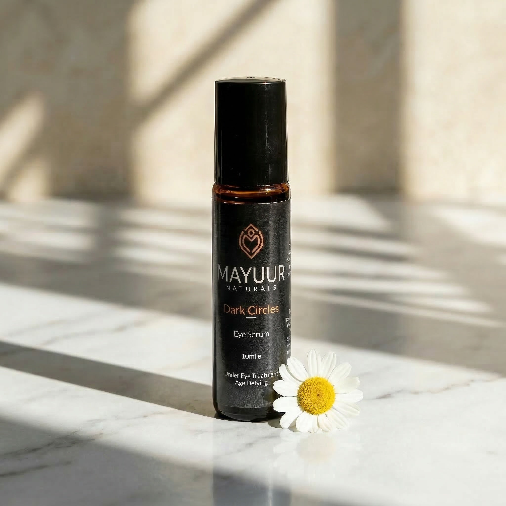 Mayuur Naturals eye serum bottle on a marble surface with a white flower.