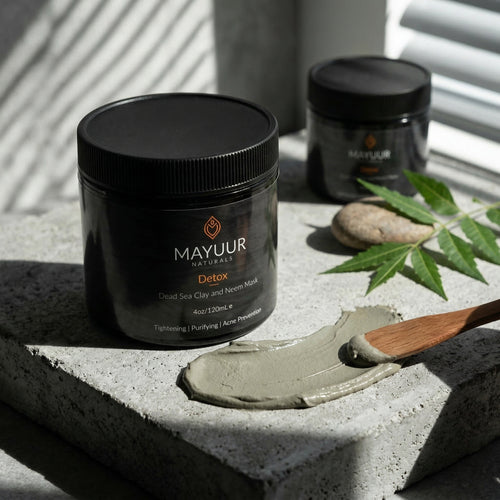 Mayuur Detox mask jar with a spoonful of mask on a stone surface with leaves.