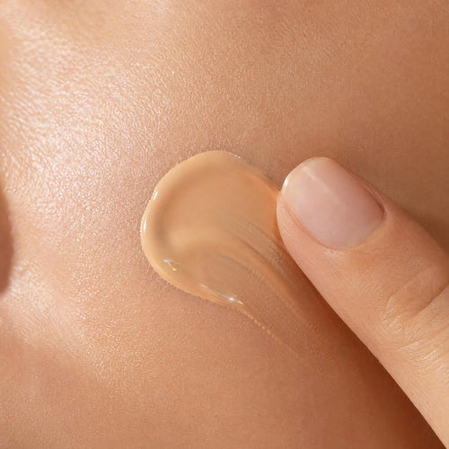 Close-up of a hand applying beige cream to skin
