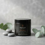 Black jar of Mayuur Fresh Waters body butter on a gray surface with eucalyptus leaves.