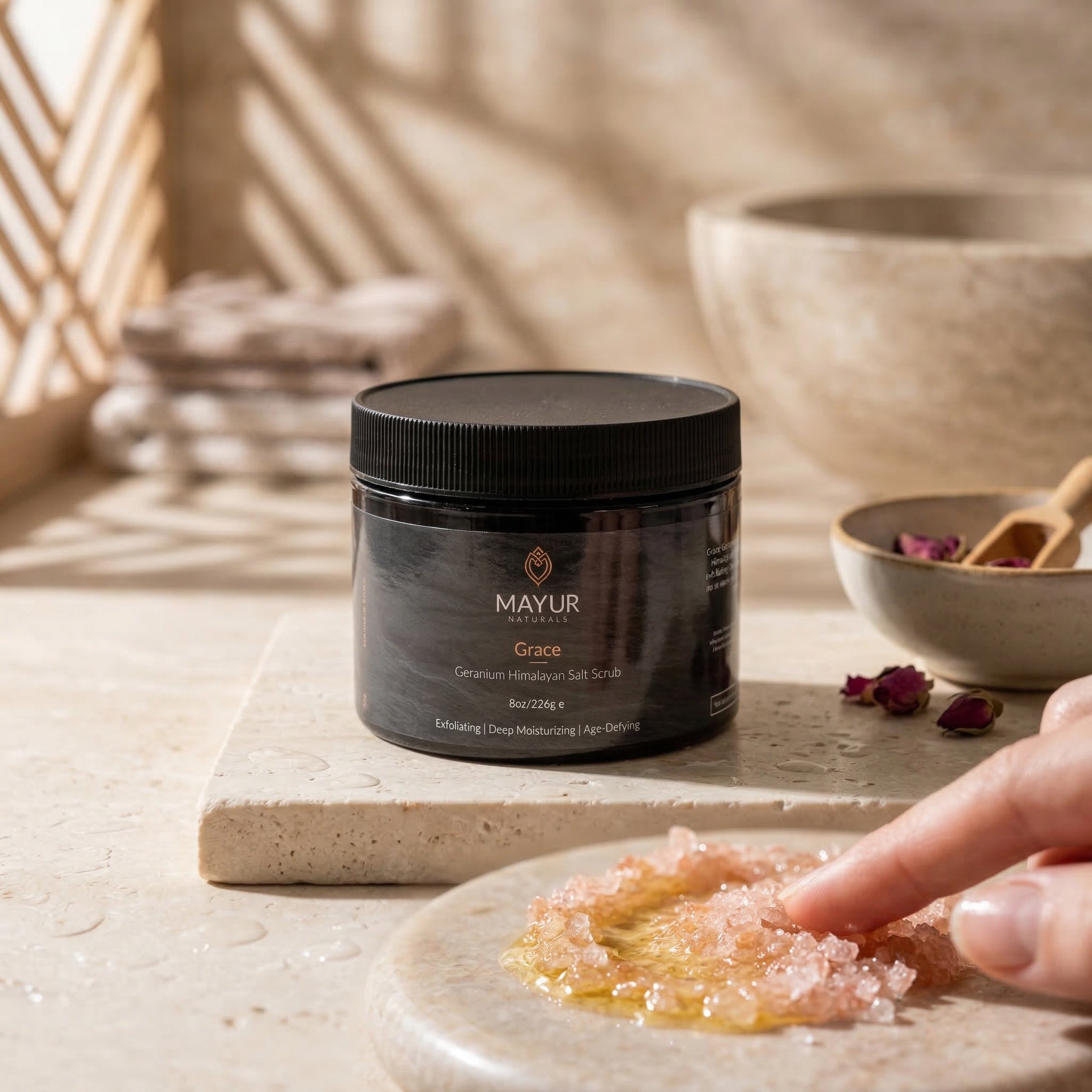Mayur Gace scrub jar on a stone surface with a hand holding a bowl of scrub.