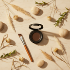 Makeup compact with brush on a beige surface with dried plants and stones