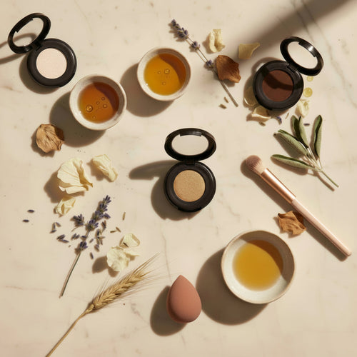 Makeup products including eyeshadows and a brush on a light surface with natural elements.